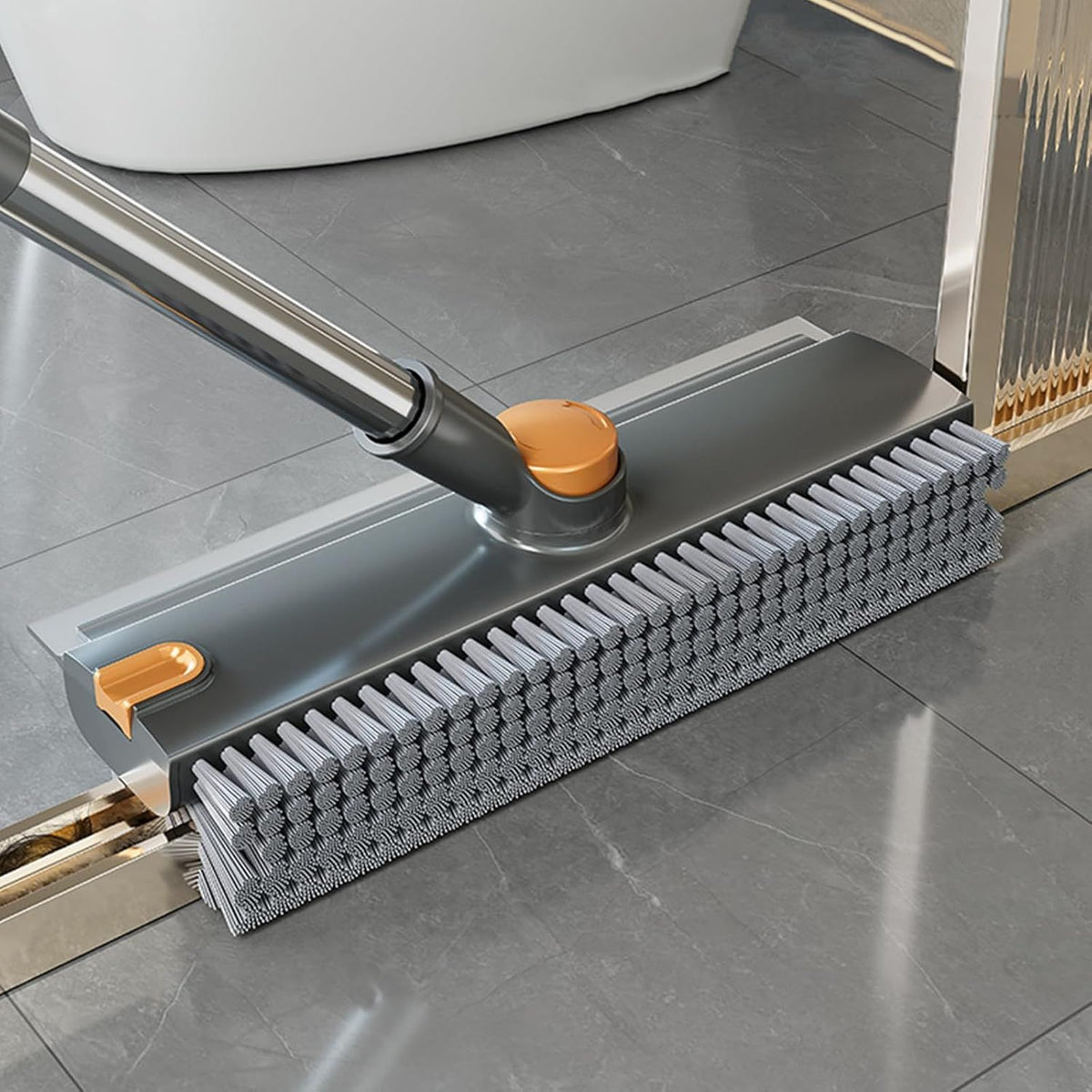 Floor cleaning tool with a gray brush head and orange handles on a tiled floor.