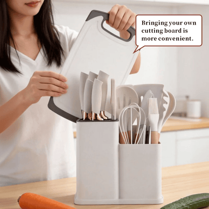 A woman in a white shirt places a white cutting board into a white kitchen utensil organizer on a wooden countertop. The organizer contains knives, spoons, a whisk, and a brush.