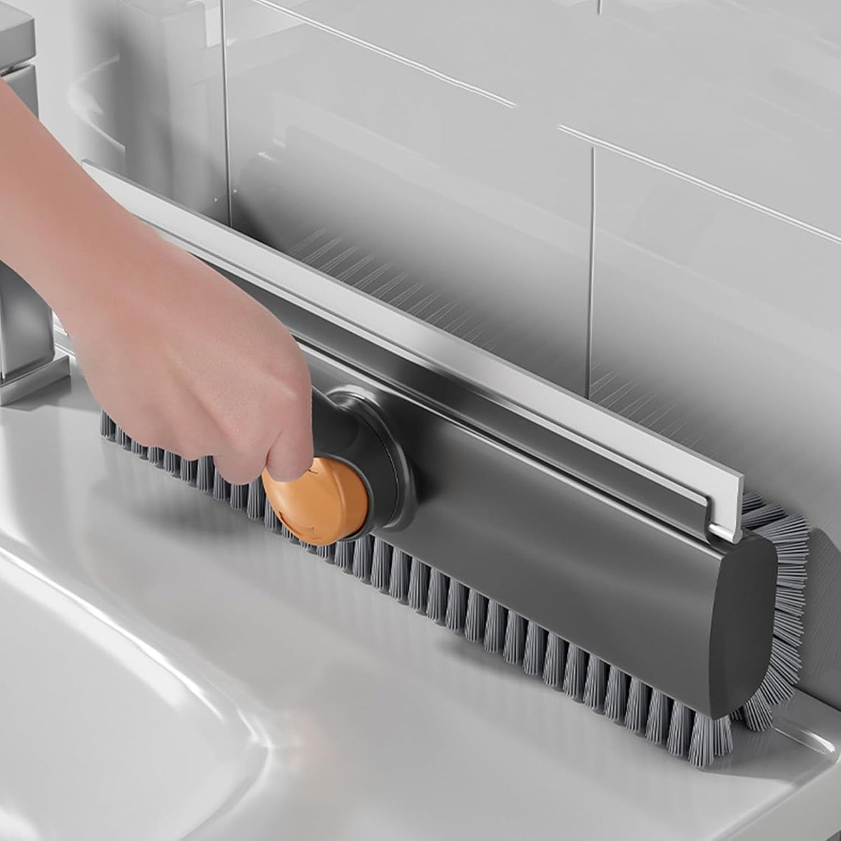 Gray scrub brush with orange handle being used to clean under a kitchen sink.